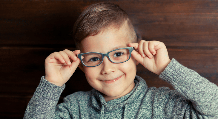 Child smiles in front of wood wall. 